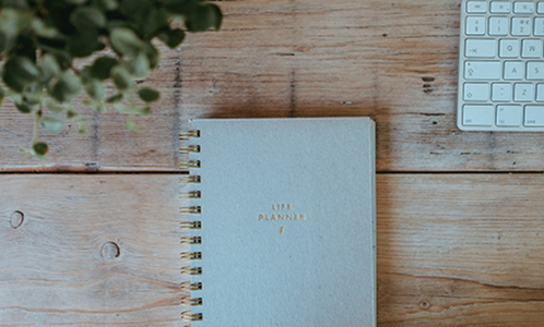Carnet posé sur une table en bois avec un clavier d’ordinateur et une plante floutée, illustrant la création et l’optimisation d’un site web. conseils webdesign et création de site internet.